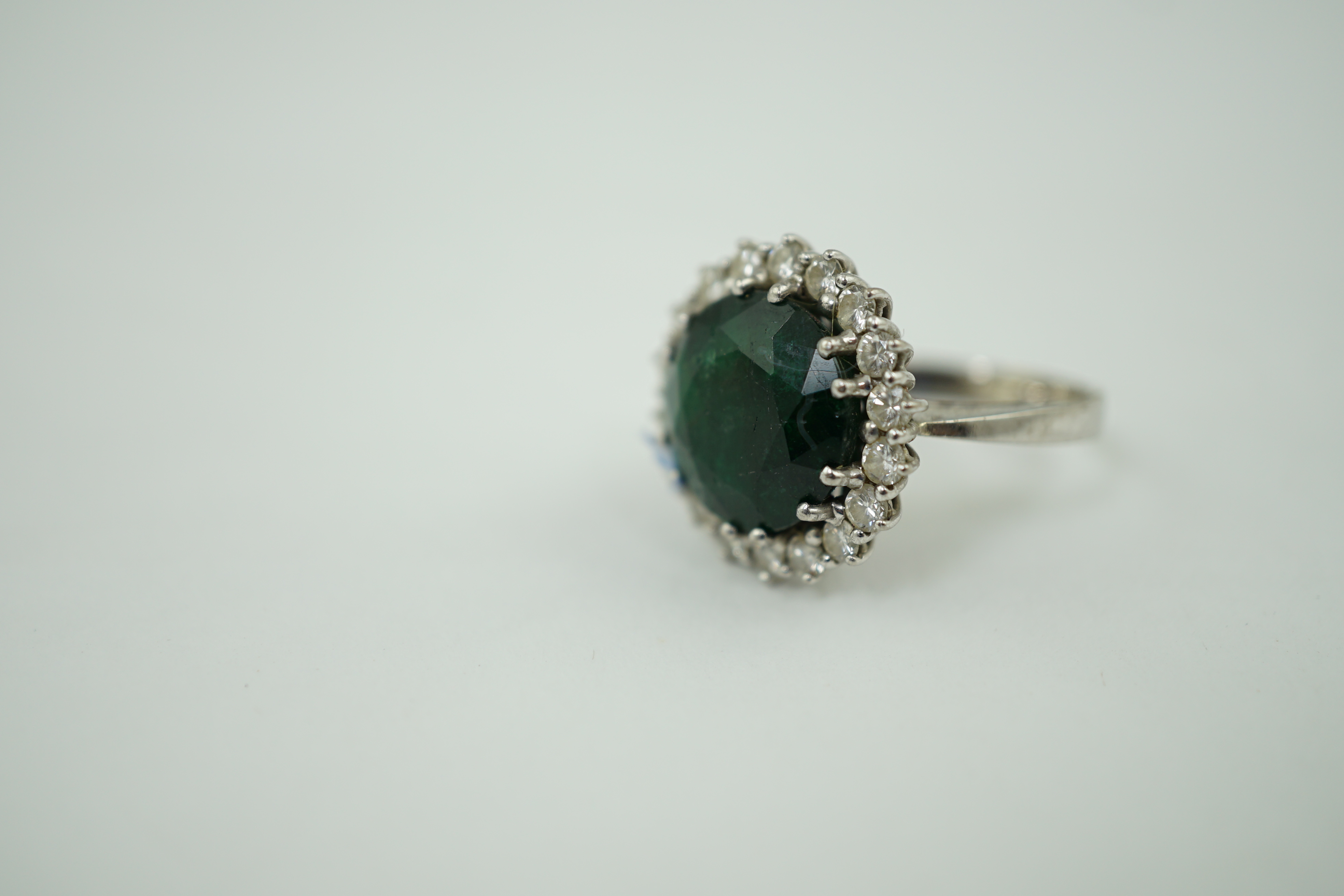 A mid 20th century 18k white gold and round cut emerald set dress ring, with diamond set border